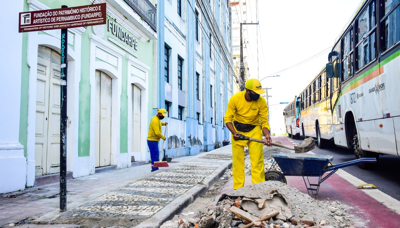 Trabalhador de uniforme amarelo faz reparo na calçada em frente à FUNDARPE. Mais na postagem